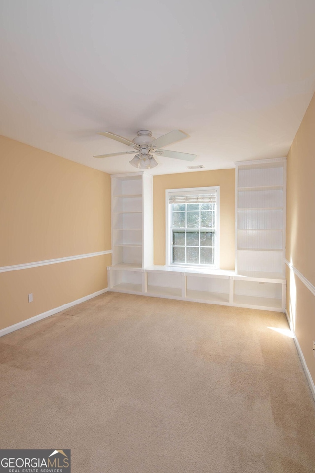 carpeted spare room with built in shelves, visible vents, ceiling fan, and baseboards