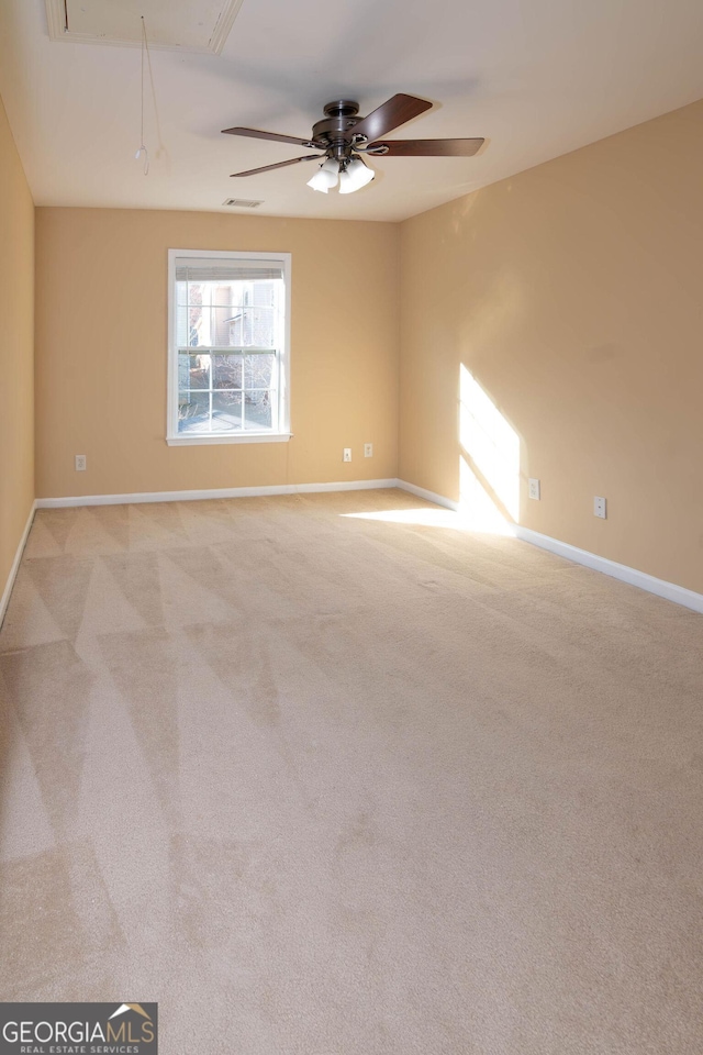 unfurnished room with light colored carpet, visible vents, attic access, a ceiling fan, and baseboards