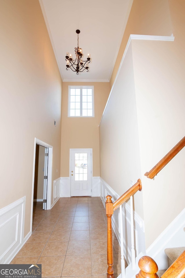 entryway featuring light tile patterned floors, a decorative wall, an inviting chandelier, ornamental molding, and stairs