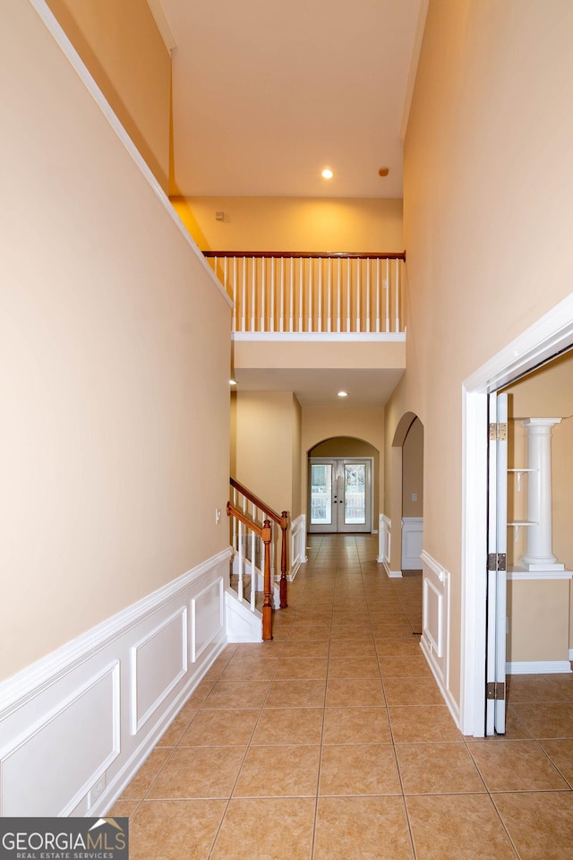 hall with arched walkways, light tile patterned floors, a decorative wall, stairs, and french doors