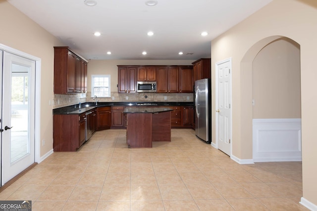 kitchen featuring light tile patterned floors, tasteful backsplash, dark countertops, appliances with stainless steel finishes, and a center island