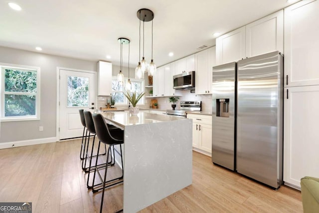 kitchen featuring a kitchen breakfast bar, light wood-style floors, white cabinets, appliances with stainless steel finishes, and decorative backsplash