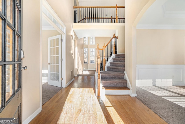 entrance foyer with ornamental molding, french doors, a towering ceiling, and wood finished floors