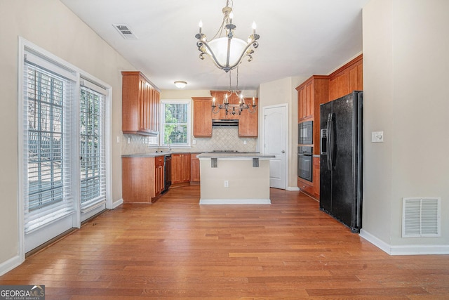 kitchen with light wood finished floors, visible vents, a kitchen island, black appliances, and a chandelier