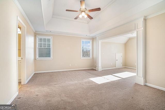 spare room with a tray ceiling, light colored carpet, ornamental molding, ceiling fan, and baseboards