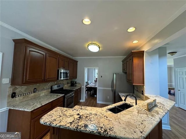 kitchen with stainless steel appliances, a peninsula, a sink, backsplash, and dark wood finished floors