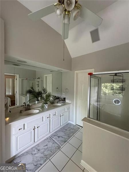 full bath with double vanity, a stall shower, ceiling fan, vaulted ceiling, and a sink