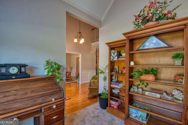 sitting room with a wainscoted wall, wood finished floors, an inviting chandelier, crown molding, and a decorative wall