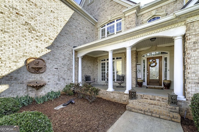 view of exterior entry featuring a porch and brick siding