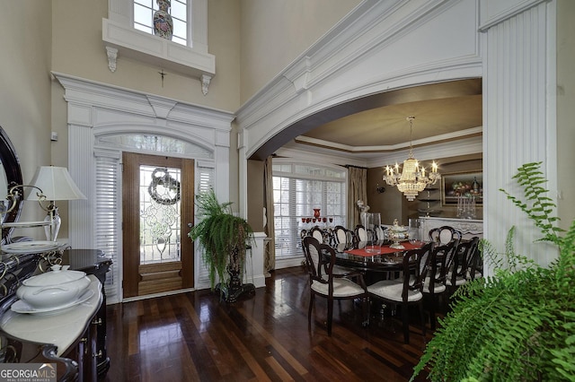 entryway featuring arched walkways, a towering ceiling, ornamental molding, hardwood / wood-style floors, and an inviting chandelier