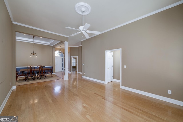 unfurnished living room with ceiling fan with notable chandelier, baseboards, light wood-style floors, ornamental molding, and a tray ceiling