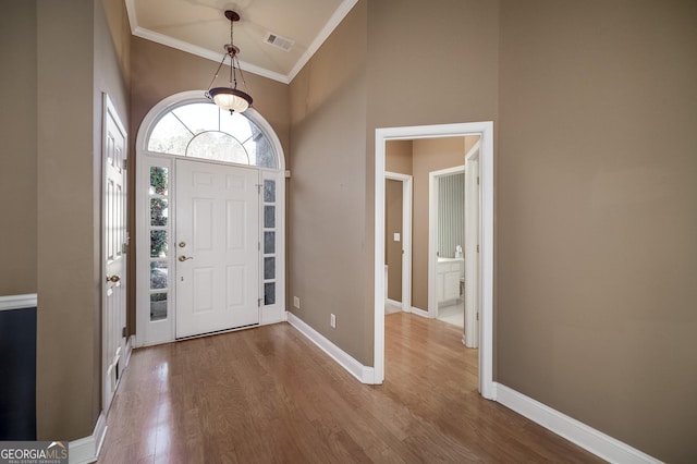 foyer entrance with wood finished floors, a towering ceiling, visible vents, baseboards, and crown molding