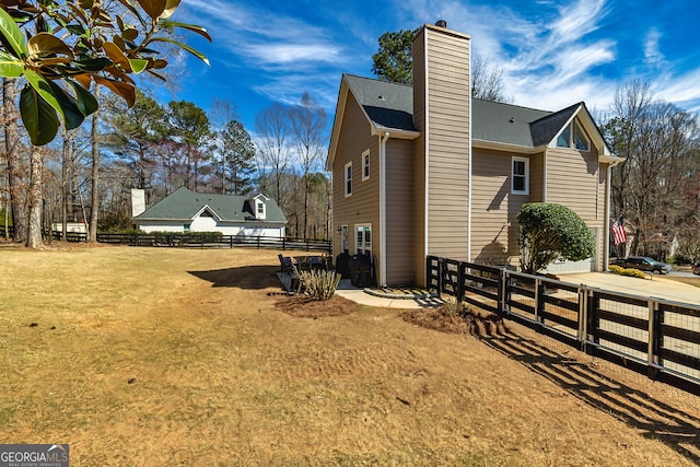 view of property exterior with a chimney, fence, and a lawn