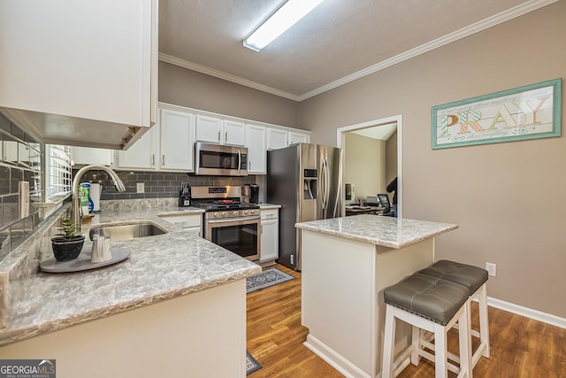 kitchen featuring a kitchen breakfast bar, a sink, stainless steel appliances, white cabinetry, and backsplash