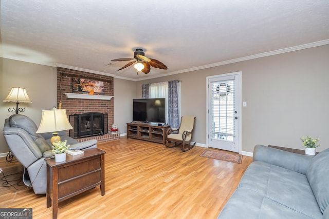 living area with crown molding, a fireplace, light wood finished floors, a ceiling fan, and baseboards