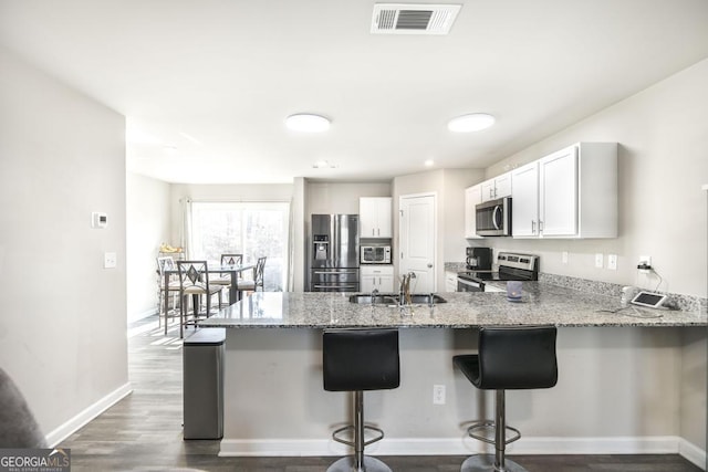 kitchen featuring light stone counters, stainless steel appliances, a peninsula, a sink, and visible vents