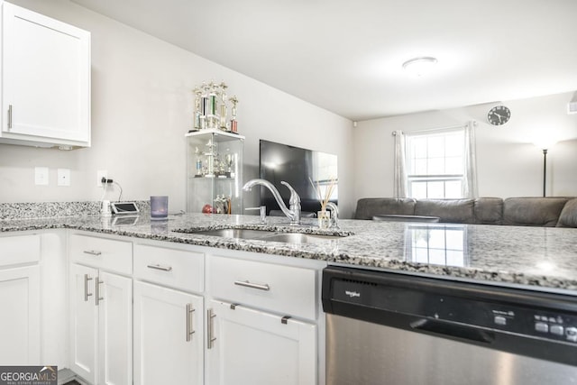 kitchen with white cabinets, light stone counters, open floor plan, stainless steel dishwasher, and a sink