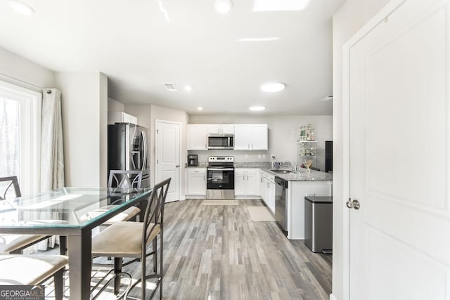 kitchen with light stone counters, recessed lighting, light wood-style flooring, appliances with stainless steel finishes, and white cabinets