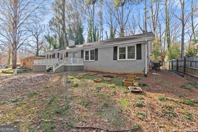 ranch-style house with a deck, brick siding, a chimney, and fence