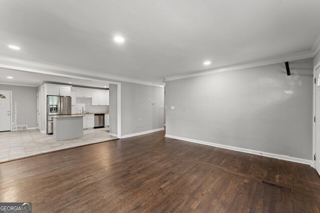 unfurnished living room featuring ornamental molding, wood finished floors, visible vents, and baseboards