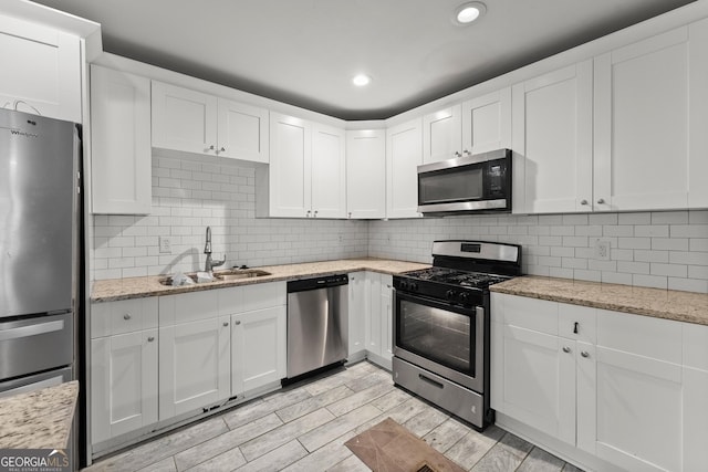 kitchen featuring decorative backsplash, appliances with stainless steel finishes, white cabinetry, a sink, and light wood-type flooring