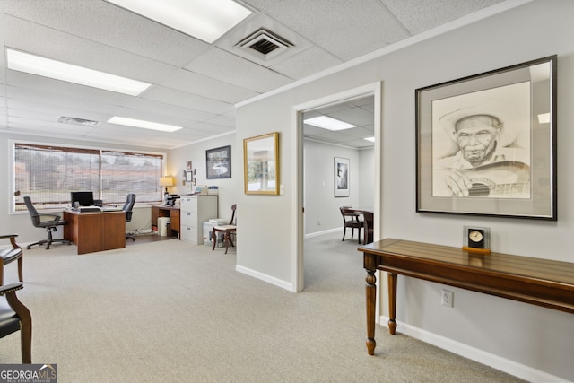 office space featuring baseboards, a paneled ceiling, visible vents, and light colored carpet