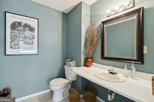 bathroom featuring baseboards, toilet, tile patterned flooring, a textured ceiling, and a sink