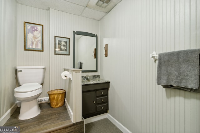 half bath featuring baseboards, visible vents, toilet, vanity, and a paneled ceiling