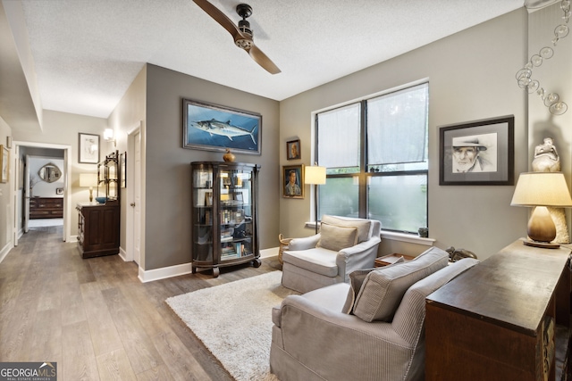 living room with light wood finished floors, ceiling fan, baseboards, and a textured ceiling