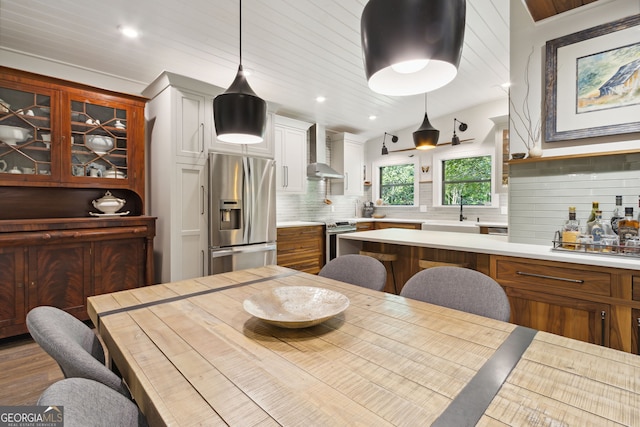 kitchen with stainless steel appliances, a sink, light countertops, wall chimney exhaust hood, and tasteful backsplash