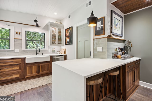 kitchen featuring visible vents, glass insert cabinets, dark wood-style flooring, a peninsula, and a sink