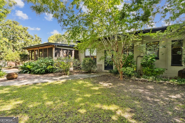 view of front facade with a sunroom, concrete block siding, and a front lawn