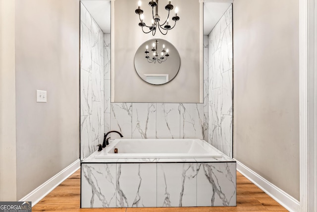 bathroom with a garden tub, baseboards, a notable chandelier, and wood finished floors