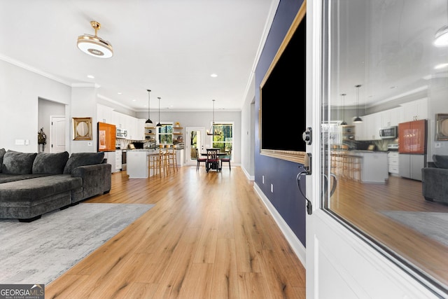 living room featuring recessed lighting, baseboards, crown molding, and light wood finished floors