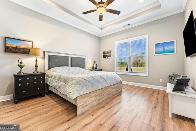 bedroom with light wood finished floors, visible vents, baseboards, a tray ceiling, and crown molding