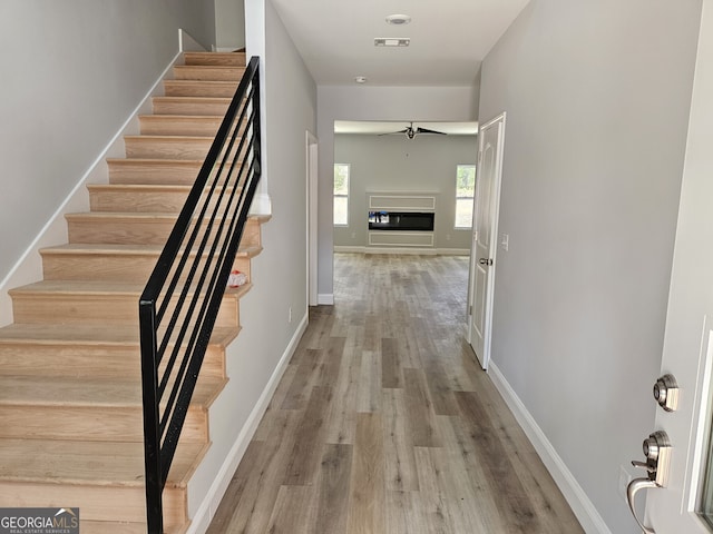 interior space with wood finished floors, a ceiling fan, baseboards, stairway, and a glass covered fireplace