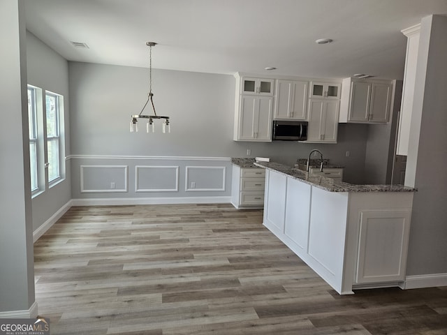 kitchen with stone countertops, white cabinetry, light wood-style floors, stainless steel microwave, and glass insert cabinets