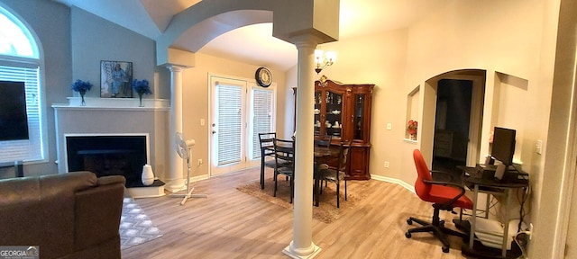 dining area with arched walkways, a fireplace with raised hearth, baseboards, light wood-type flooring, and ornate columns