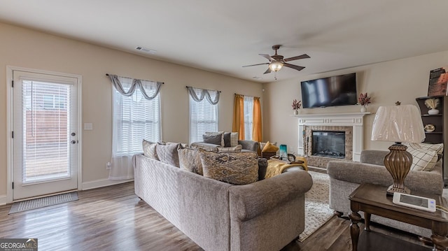 living area featuring ceiling fan, wood finished floors, visible vents, baseboards, and a glass covered fireplace