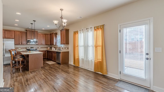 kitchen with a kitchen island, dark wood-style flooring, stainless steel appliances, light countertops, and backsplash