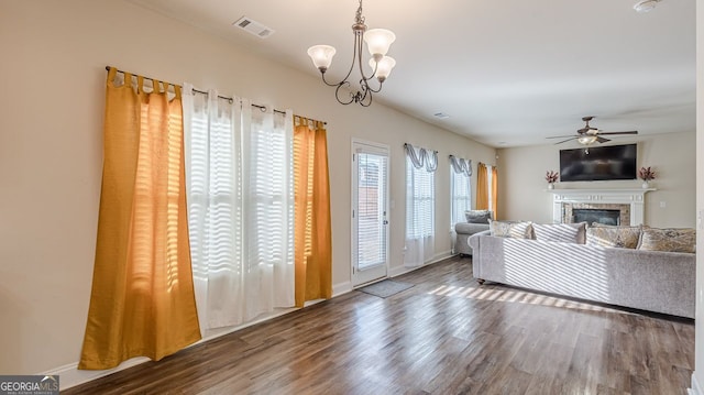 unfurnished living room featuring baseboards, visible vents, a glass covered fireplace, wood finished floors, and ceiling fan with notable chandelier