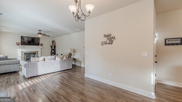 living room with ceiling fan with notable chandelier, a glass covered fireplace, baseboards, and wood finished floors