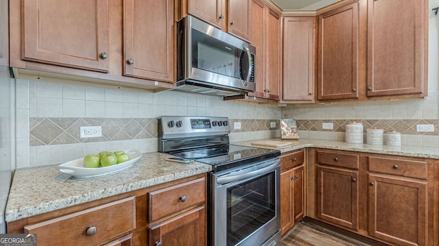 kitchen with light wood-type flooring, brown cabinetry, appliances with stainless steel finishes, and decorative backsplash