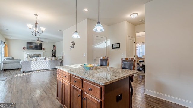 kitchen featuring a ceiling fan, dark wood-style floors, a kitchen island, hanging light fixtures, and a fireplace