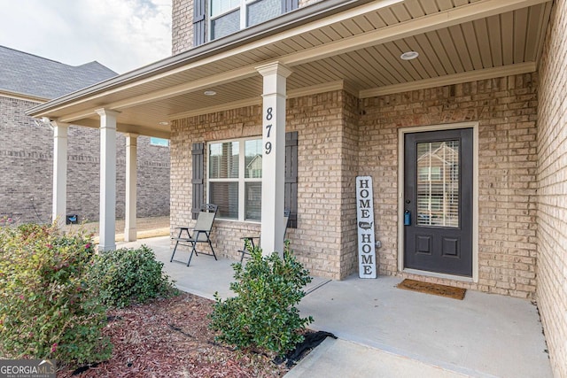 entrance to property featuring covered porch and brick siding