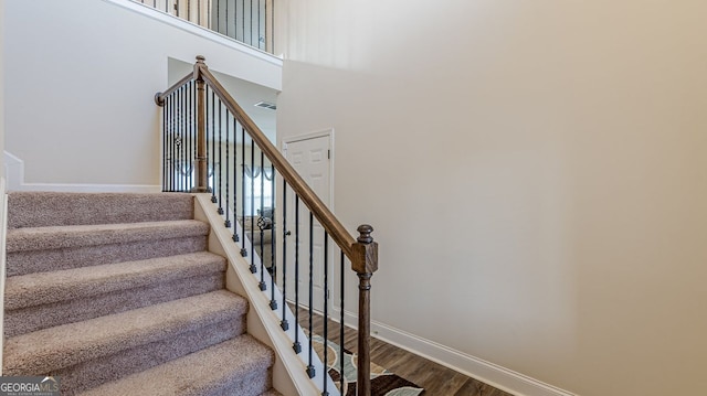 stairway with a towering ceiling, visible vents, baseboards, and wood finished floors