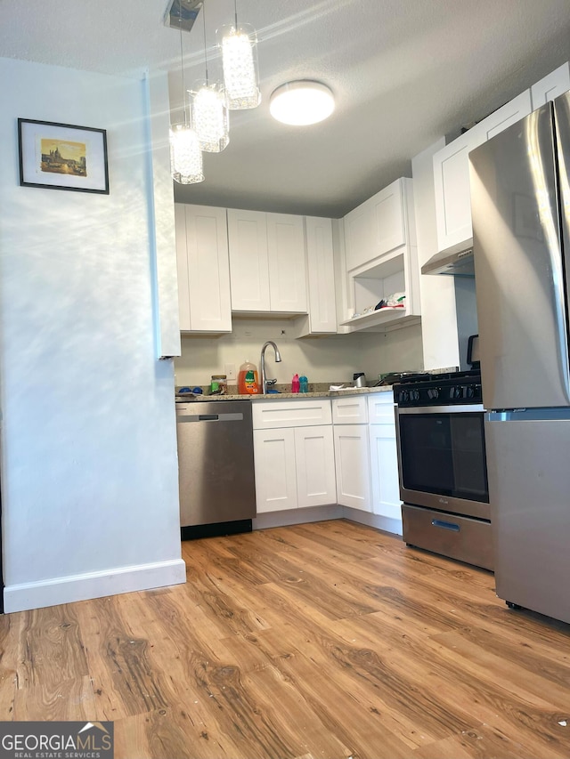 kitchen with white cabinets, light wood-style flooring, appliances with stainless steel finishes, pendant lighting, and a sink