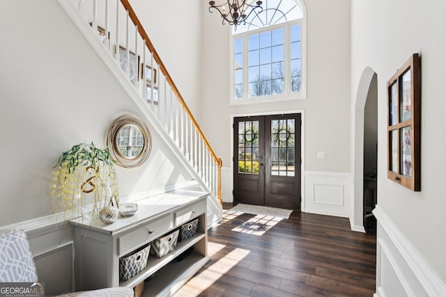 foyer with a towering ceiling, a wainscoted wall, dark wood-type flooring, stairs, and french doors