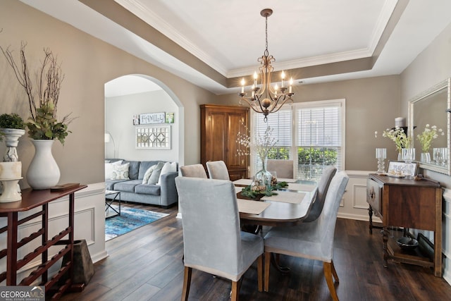 dining space with arched walkways, ornamental molding, dark wood-type flooring, a tray ceiling, and a notable chandelier