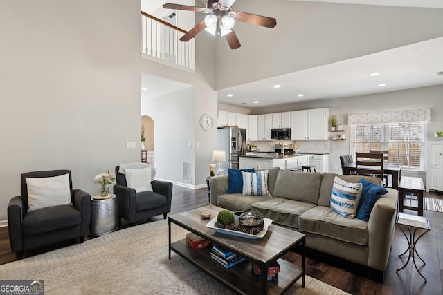 living room featuring arched walkways, recessed lighting, a high ceiling, wood finished floors, and baseboards